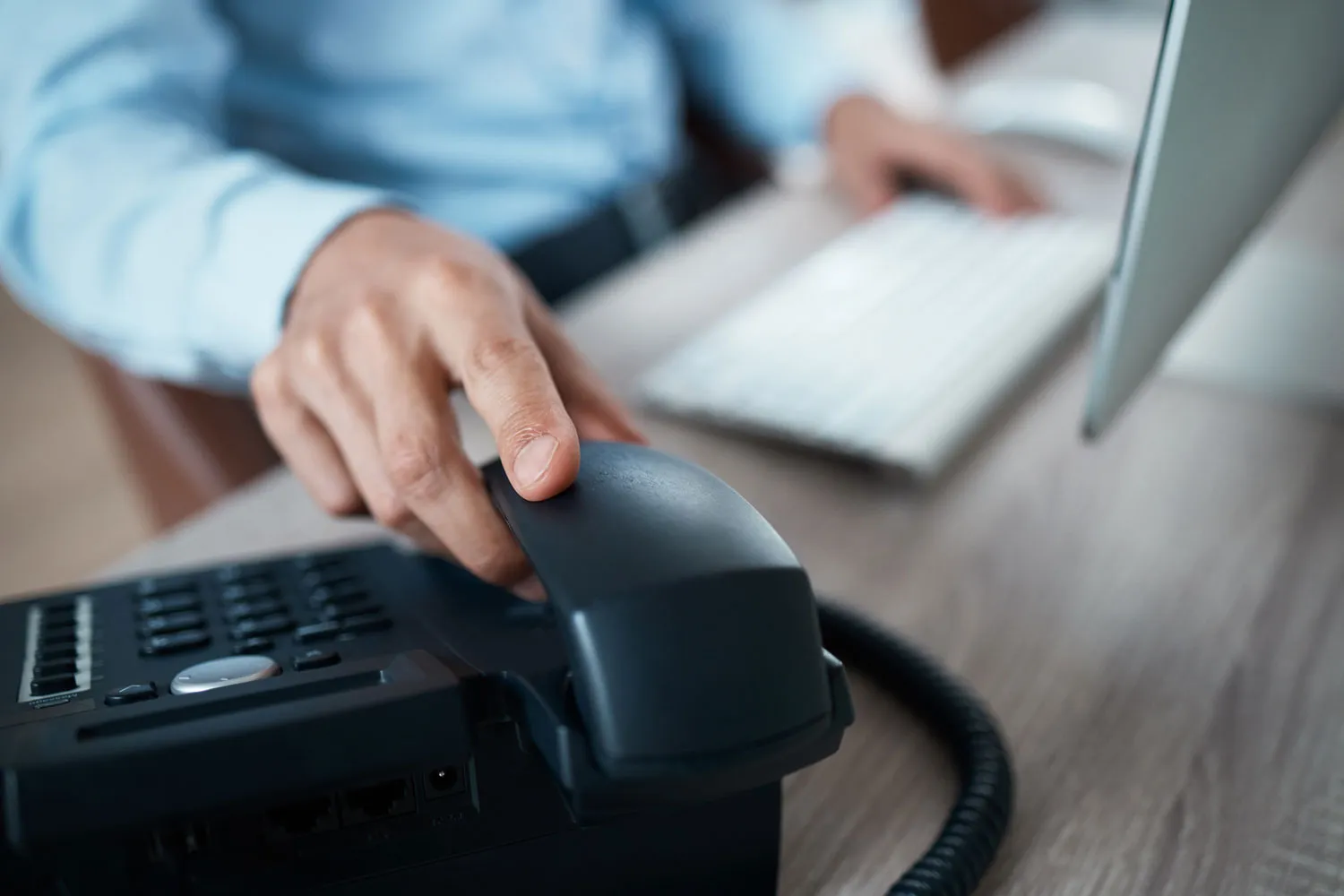 Nahaufnahme einer Hand, die ein Telefonhörer in einem Büro greift, mit einer Computertastatur im Hintergrund.